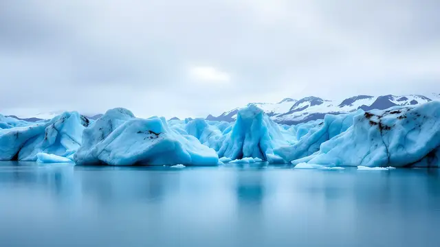 A glacier lagoon with floating blue icebergs under a soft overcast sky