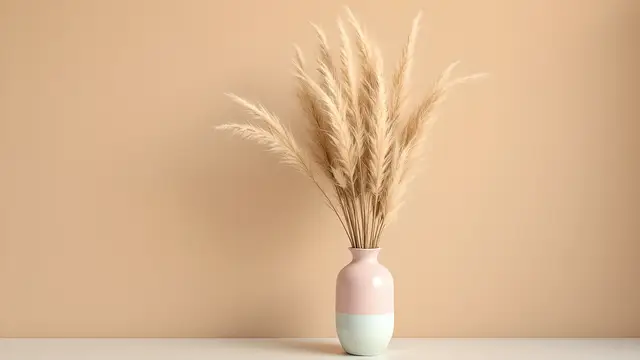A pastel ceramic vase with dried pampas grass against a beige wall