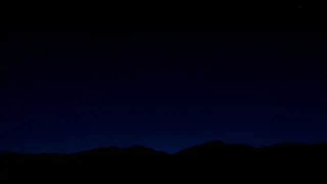 A mountain ridge silhouette under a deep blue night sky