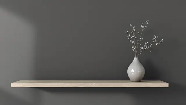 A white vase of small flowers on a pale wood shelf against a grey wall