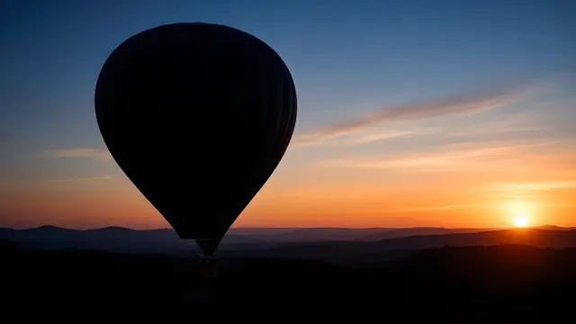 A hot air balloon silhouette over hills at dawn