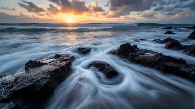 Waves washing over dark volcanic rocks at sunset